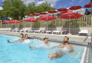 Familia divirtiéndose en la piscina con sombrillas rojas en Flower Camping Le Conleau, Bretaña, Francia.