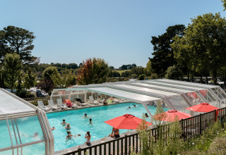 Buitenzwembad met doorzichtig dak, rode parasols en spelende vakantiegangers in een park in Bretagne, Frankrijk.