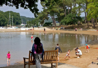 Huéspedes disfrutan de la playa de arena y el agua poco profunda en Flower Camping Le Conleau en Bretaña, Francia.