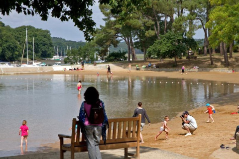 Huéspedes disfrutan de la playa de arena y el agua poco profunda en Flower Camping Le Conleau en Bretaña, Francia.