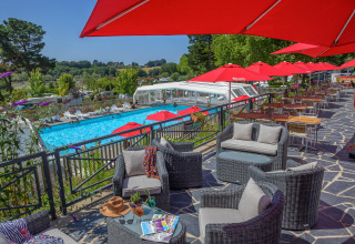 Terrace with lounge area, red umbrellas, and pool view at Flower Camping Le Conleau in Brittany, France.