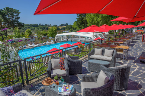 Terrazza con area lounge, ombrelloni rossi e vista sulla piscina al Flower Camping Le Conleau in Bretagna.