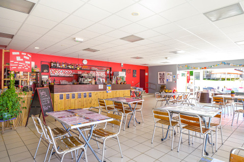 Zona luminosa de cafetería en Flower Camping Le Conleau, Bretaña, Francia, con mesas, sillas y barra.
