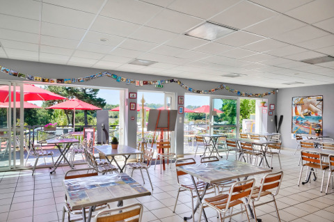 Luminoso comedor en Flower Camping Le Conleau, Bretaña, Francia, con vistas a terraza y sombrillas rojas.
