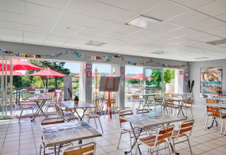 Luminoso comedor en Flower Camping Le Conleau, Bretaña, Francia, con vistas a terraza y sombrillas rojas.