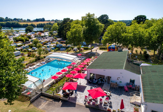 Vista aérea de Flower Camping Le Conleau en Bretaña, Francia, con piscina, sombrillas rojas y caravanas.