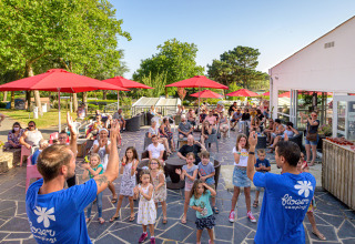 Familien genießen Aktivitäten bei Flower Camping Le Conleau in der Bretagne, Frankreich, unter roten Sonnenschirmen.