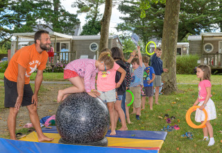 Niños juegan y se equilibran sobre una bola grande en el parque vacacional Flower Camping Le Conleau, supervisados por un adulto.