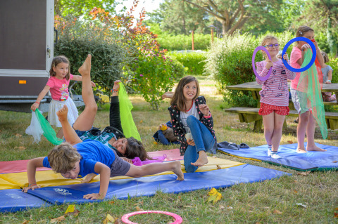 Niños juegan y hacen gimnasia en colchonetas al aire libre en Flower Camping Le Conleau, un parque vacacional en Bretaña, Francia.