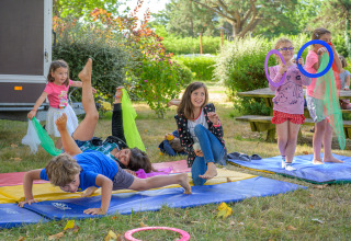 Niños juegan y hacen gimnasia en colchonetas al aire libre en Flower Camping Le Conleau, un parque vacacional en Bretaña, Francia.