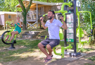 Two people using outdoor fitness equipment at Flower Camping Le Conleau holiday park in Brittany, France.