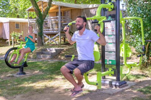 Two people using outdoor fitness equipment at Flower Camping Le Conleau holiday park in Brittany, France.