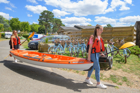 Twee vrouwen dragen een oranje kajak langs fietsen bij Flower Camping Le Conleau in Bretagne, Frankrijk.