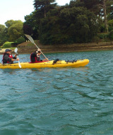 To personer padler i en gul kajak på vandet ved Flower Camping Le Conleau i Bretagne, Frankrig.
