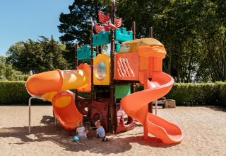 Bunter Spielplatz mit Rutschen und zwei Kindern, die im Sand im Flower Camping Le Conleau, Bretagne, spielen.