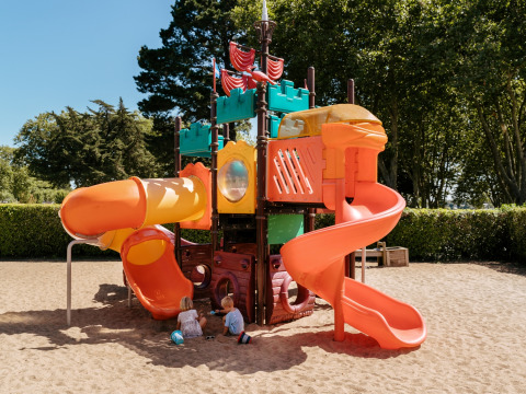 Bunter Spielplatz mit Rutschen und zwei Kindern, die im Sand im Flower Camping Le Conleau, Bretagne, spielen.