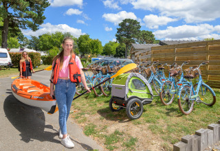 Due donne portano un kayak accanto a biciclette e un rimorchio in un campeggio in Bretagna, Francia.