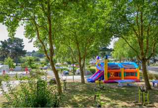 Playground with colorful bouncy castle among trees at Flower Camping Le Conleau holiday park in Brittany, France.