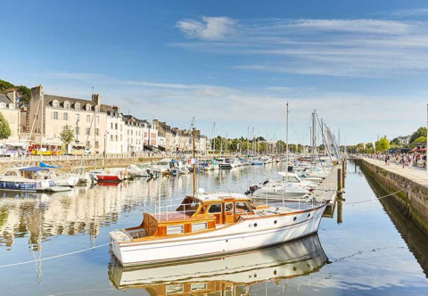 Bateaux amarrés dans un port pittoresque avec des maisons historiques et un ciel bleu en arrière-plan.