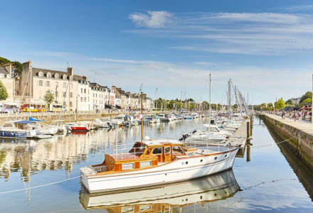 Både og sejlbåde i en idyllisk havn med smukke huse i baggrunden under en klar blå himmel.
