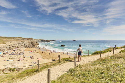 Vista de una playa de arena con gente junto al mar desde un sendero en un parque vacacional con glamping.
