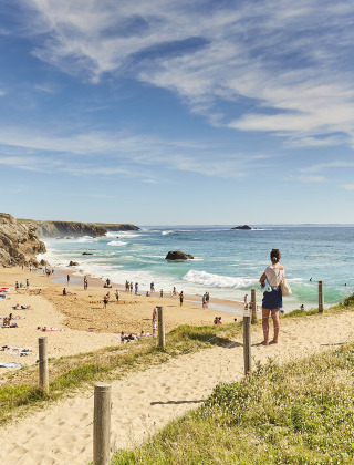 Blick auf einen Sandstrand mit vielen Menschen am Meer, gesehen von einem Ferienpark mit Glampingbereich.
