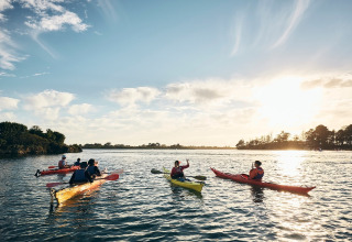 Un grupo de personas hace kayak al atardecer en un lago cerca de un glamping rodeado de naturaleza.