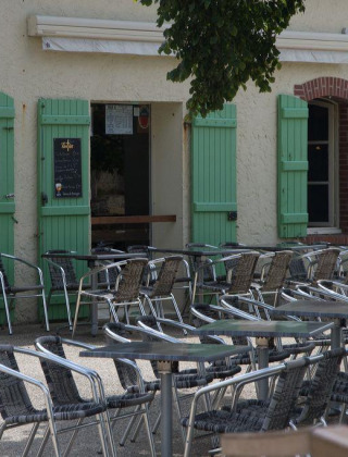 Udendørs café nær Vannes i Bretagne, Frankrig, med tomme borde, grønne skodder og to personer.