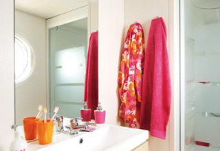 Salle de bain d’un hébergement glamping avec serviettes colorées, vasque moderne et douche vitrée.