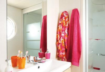 Salle de bain d’un hébergement glamping avec serviettes colorées, vasque moderne et douche vitrée.