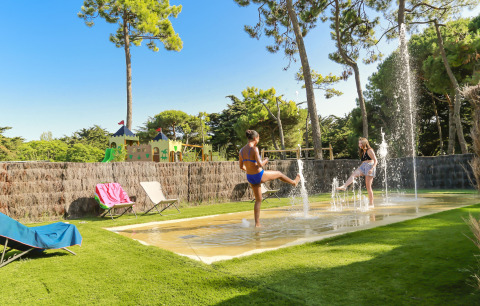 Dos niños juegan en fuentes de agua sobre césped en Flower Camping Tamarins Plage, Nueva Aquitania, Francia.