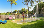 Twee kinderen spelen in waterstralen op het gras bij Flower Camping Tamarins Plage in Frankrijk.