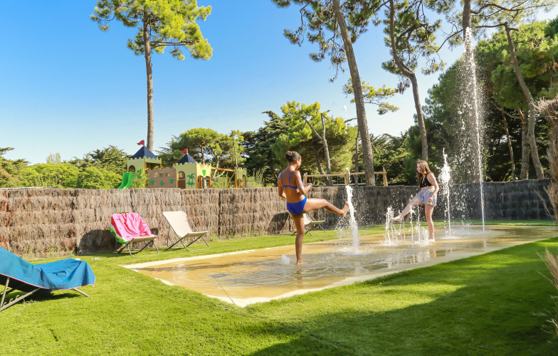 Zwei Kinder spielen in Springbrunnen auf einer Wiese im Flower Camping Tamarins Plage, Nouvelle-Aquitaine.