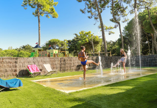 Zwei Kinder spielen in Springbrunnen auf einer Wiese im Flower Camping Tamarins Plage, Nouvelle-Aquitaine.