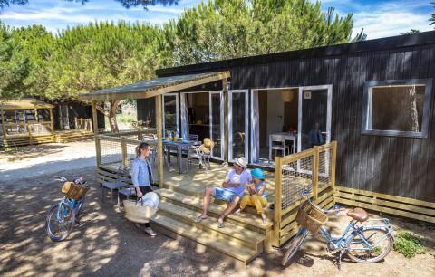 Familia disfruta en el porche de un alojamiento glamping Stacaravan Premium, rodeado de árboles y bicicletas.