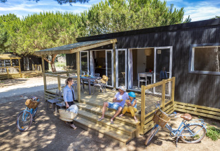 Een gezin geniet op het terras van een Stacaravan Premium glamping, omringd door fietsen en natuur.