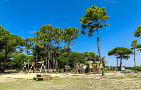 Spielplatz mit Schaukeln und Kletterburg im Flower Camping Tamarins Plage, umgeben von Kiefern.