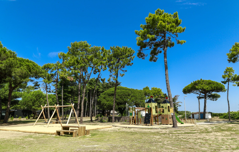 Parco giochi con altalene e castello al Flower Camping Tamarins Plage, circondato da pini.