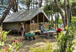 Gezin geniet bij een Tente Lodge Confort safaritent op Flower Camping Tamarins Plage in Frankrijk, tussen bomen.