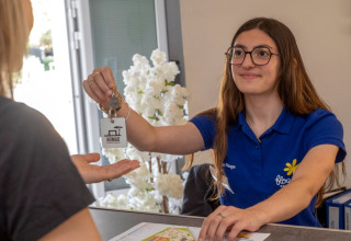 Receptioniste geeft sleutel aan gast bij Flower Camping Tamarins Plage in Nouvelle-Aquitaine, Frankrijk.