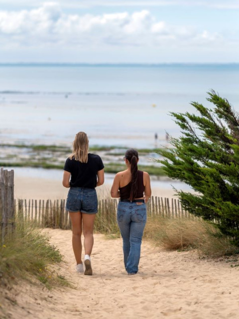 Dos mujeres caminan por un sendero de arena hacia el mar en Flower Camping Tamarins Plage, Nouvelle-Aquitaine, Francia.