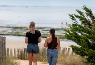 Two women walk down a sandy path towards the sea at Flower Camping Tamarins Plage in Nouvelle-Aquitaine, France.