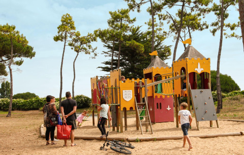 Bambini giocano su un parco giochi a tema castello sorvegliati da adulti tra gli alberi a Tamarins Plage.