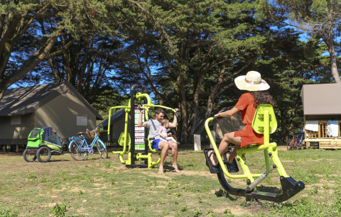 Family using outdoor gym equipment near tents and bikes at Flower Camping Tamarins Plage holiday park.