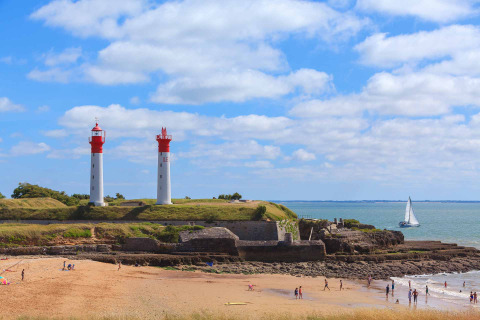 Beach scene with two lighthouses and a sailboat at Flower Camping Tamarins Plage, Nouvelle-Aquitaine, France.