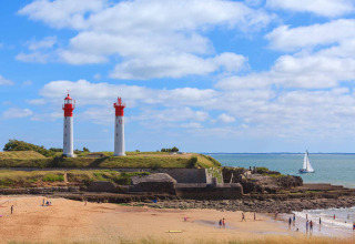 Strandscene med to fyrtårne og sejlskib ved Flower Camping Tamarins Plage i Nouvelle-Aquitaine, Frankrig.