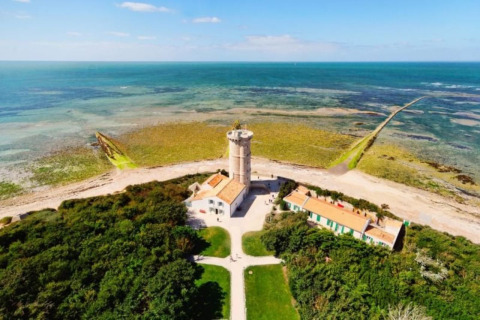 Vista aerea di un faro vicino a Le Bois-Plage-en-Ré, Francia, circondato da mare e vegetazione.