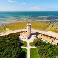 Vue aérienne d’un phare près de Le Bois-Plage-en-Ré, entouré par la mer, la plage et la végétation.