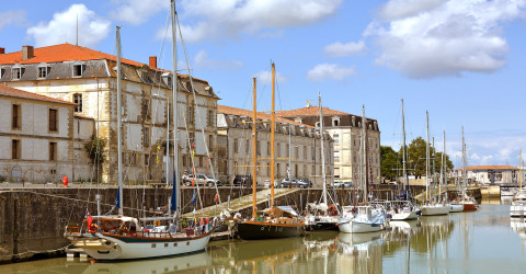 Boats moored along the canal beside historic stone buildings at Flower Camping Tamarins Plage, Nouvelle-Aquitaine.