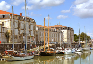 Både fortøjet ved en kanal foran historiske bygninger på Flower Camping Tamarins Plage i Nouvelle-Aquitaine.